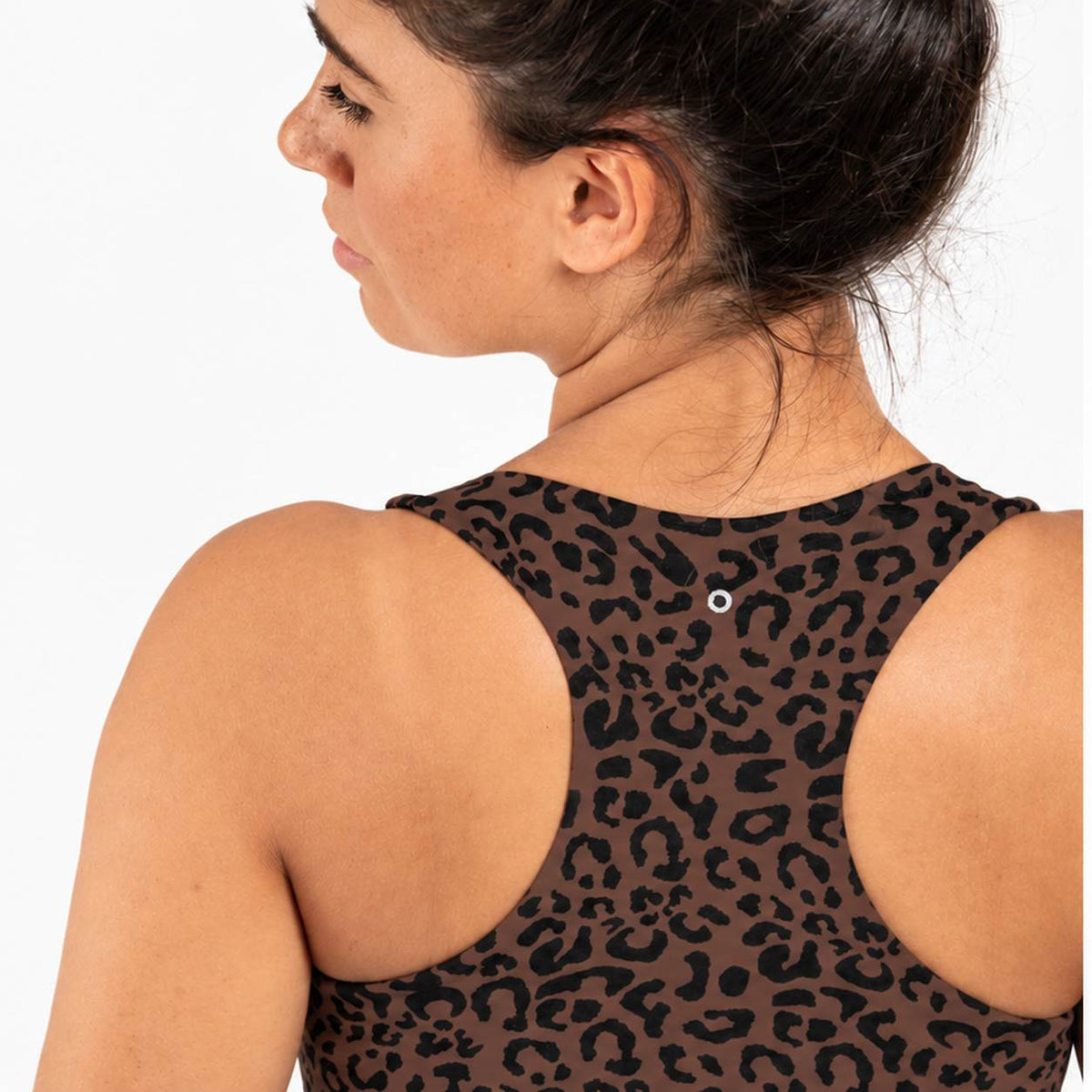 Rear three-quarter view of a woman wearing a brown and black leopard print athletic tank top, showing the open back and a small silver snap closure.