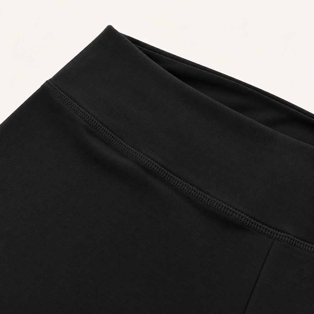 Close-up of a black organic leggings flared leggings, showing the waistband and upper front panel with a visible seam and ribbed trim against a plain light background.