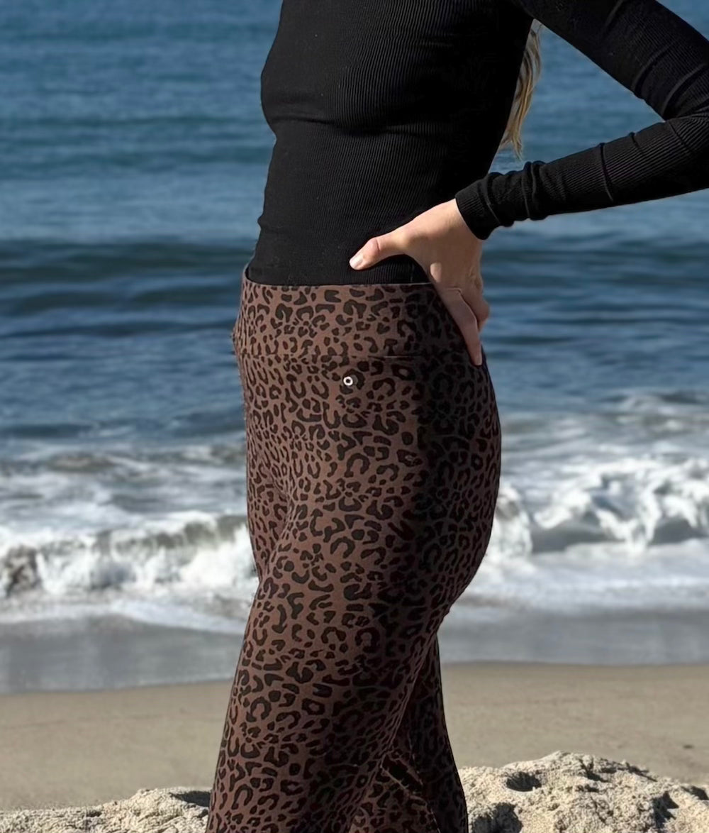 woman wearing leopard print pants and a black top on a beach 