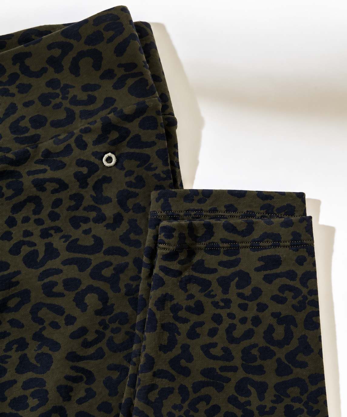 Close-up of folded leopard-print fabric in olive green and dark navy blue, with a small white circular detail visible near the top left.