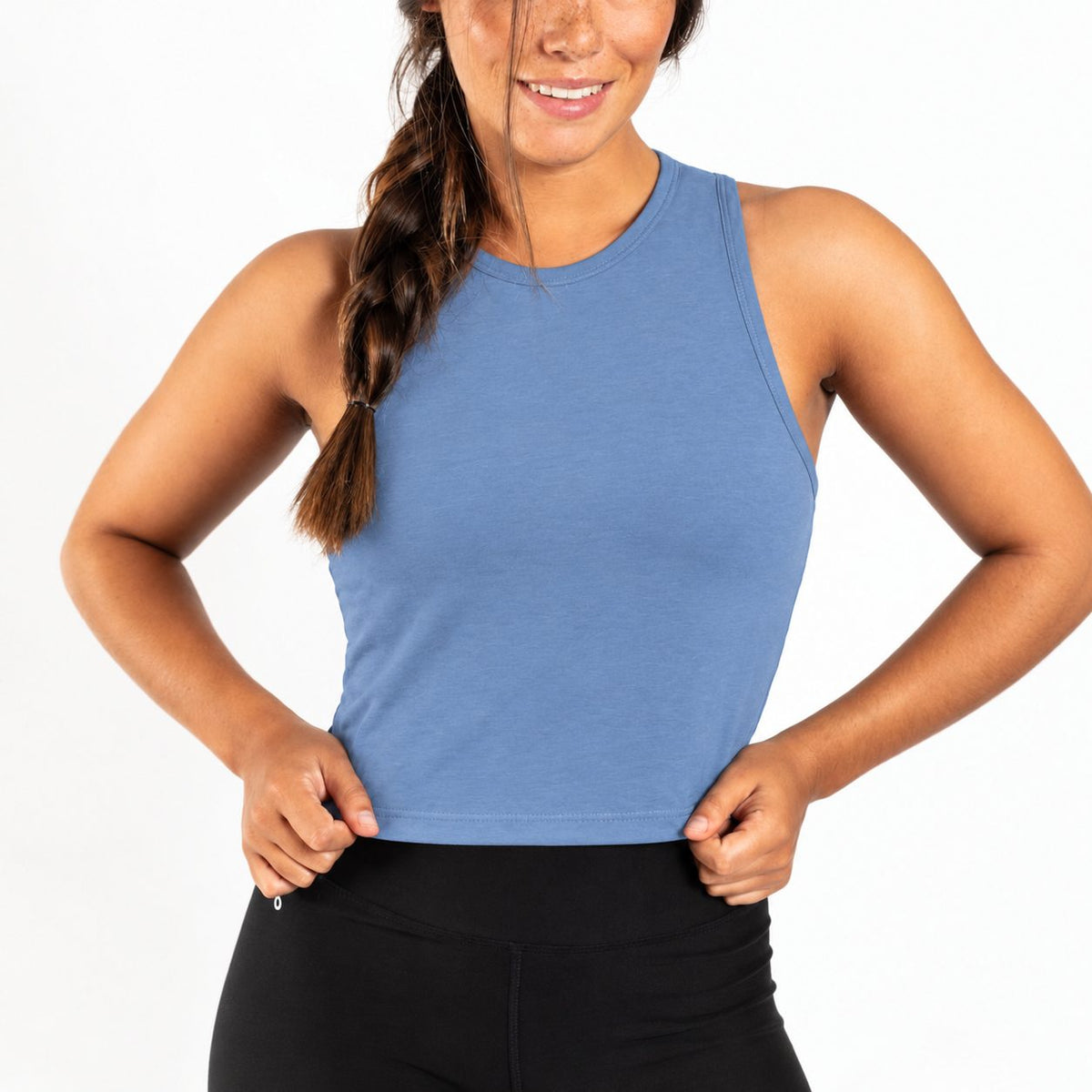 A woman wearing a sleeveless blue Organic Cotton Tank Top with built in bra  and black leggings, shown from the waist up against a plain white background.